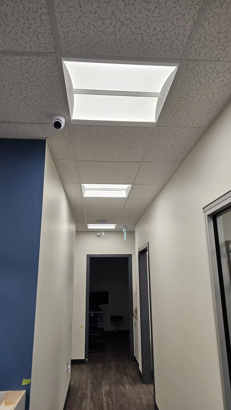 A clinic corridor installed by KeenAI with a ceiling dome camera, recessed LED troffers and a ceiling speaker in the same grid