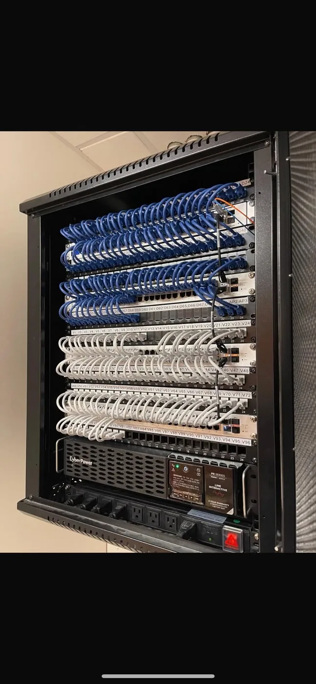 Numbered voice and data patch panels with a rack-mounted UPS, terminated and dressed by KeenAI in a commercial equipment rack