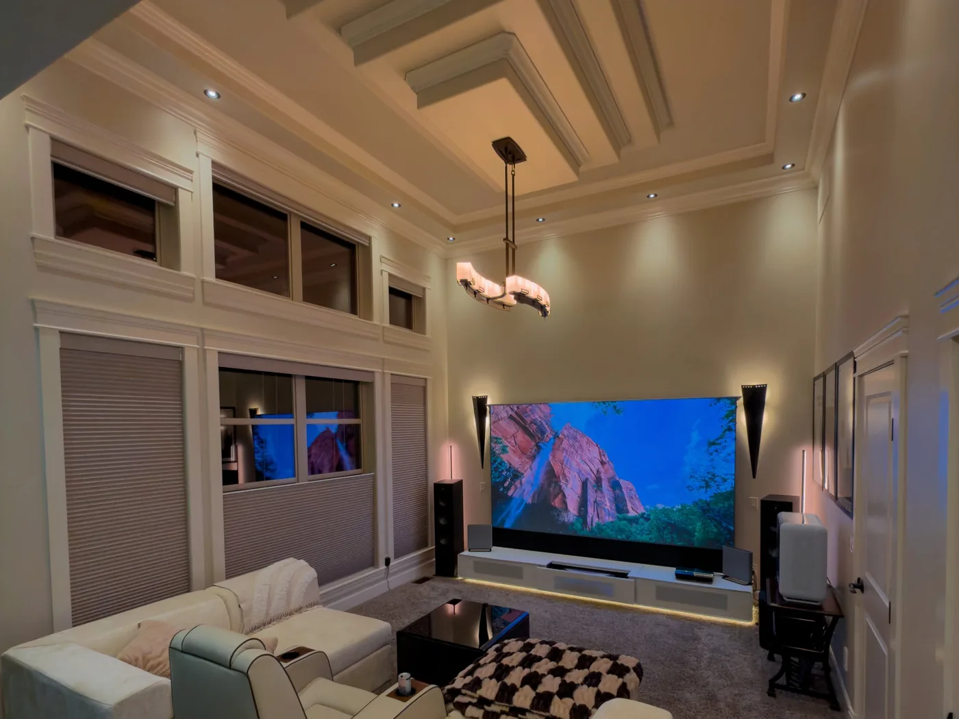 A media room installed by KeenAI, showing a coffered ceiling with recessed downlights and a pendant fitting, cellular blinds across two rows of windows, and a screen with concealed cove lighting beneath it
