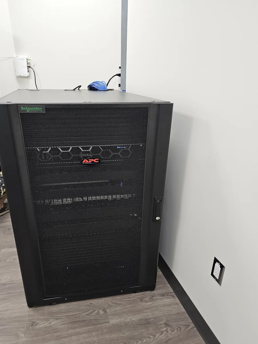 The equipment rack KeenAI installed for Eye Surgeons of Regina: a Schneider Electric APC enclosure housing a Dell server, with a ceiling access point and terminated cabling above it