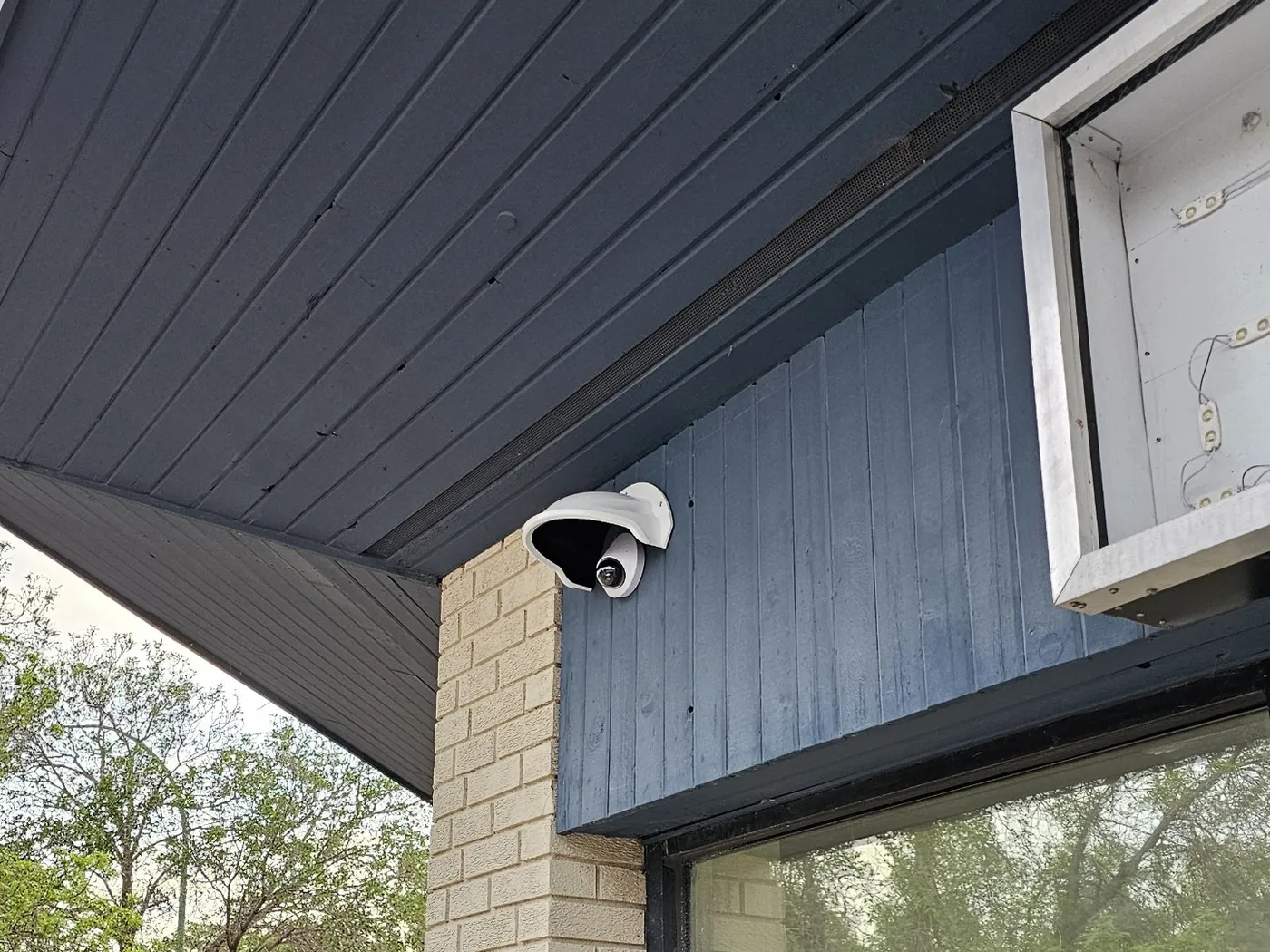 A dome security camera installed by KeenAI under the eave of a building, positioned to cover the entrance and the street beyond